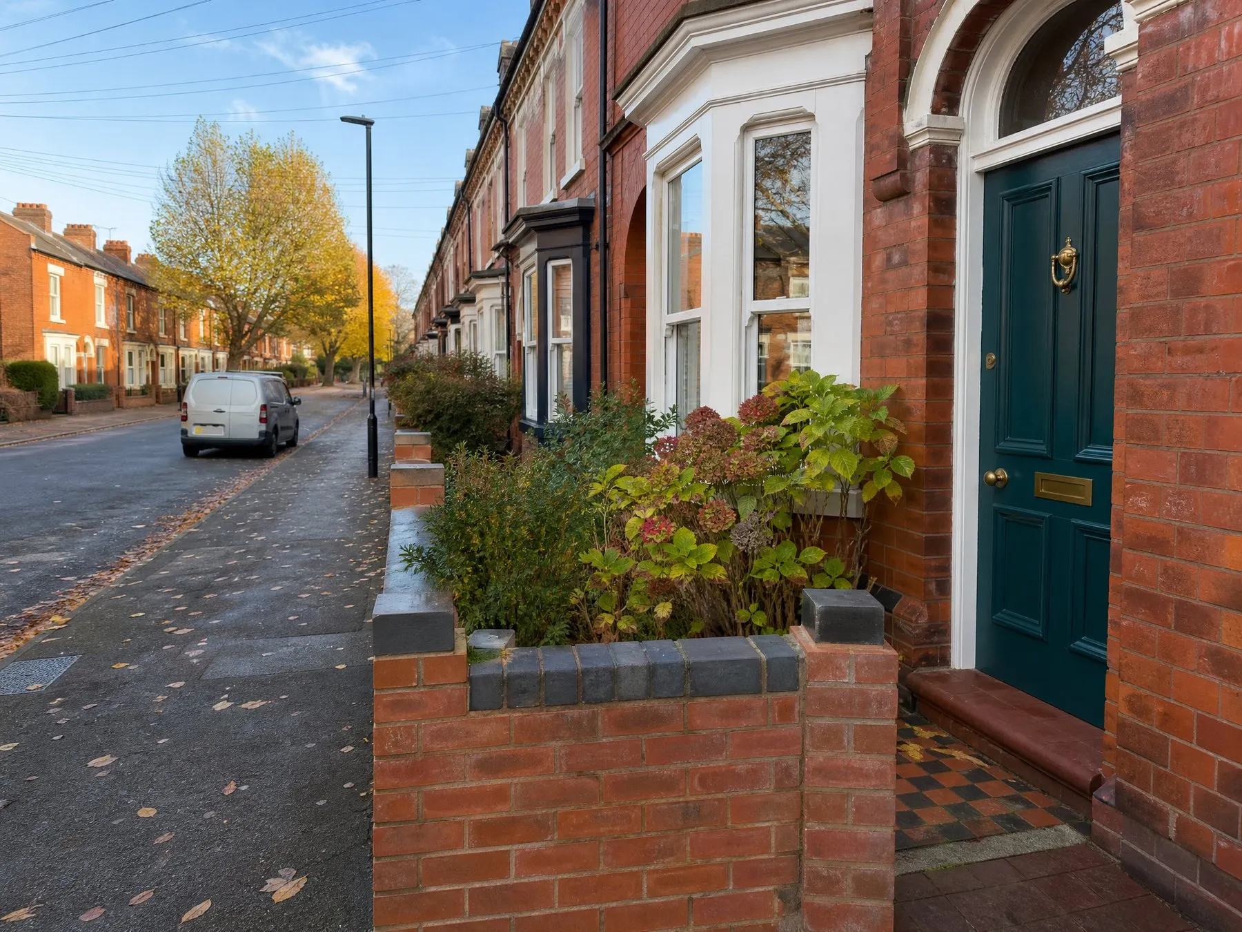 A red-brick terraced street in autumn with a teal front door